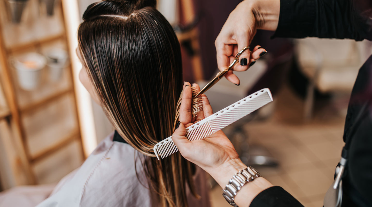 Gros plan des mains d'un professionnel tenant un peigne et un miroir lors d'une analyse capillaire en salon