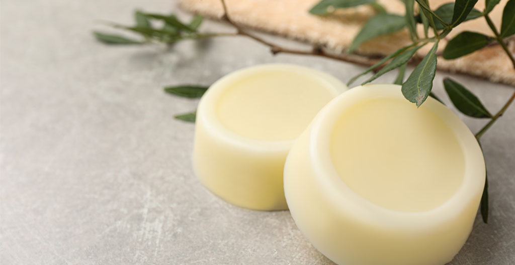 Comparaison visuelle emballages cosmétiques : empilement de flacons plastiques vides face à un shampoing solide avec emballage kraft minimal sur fond blanc